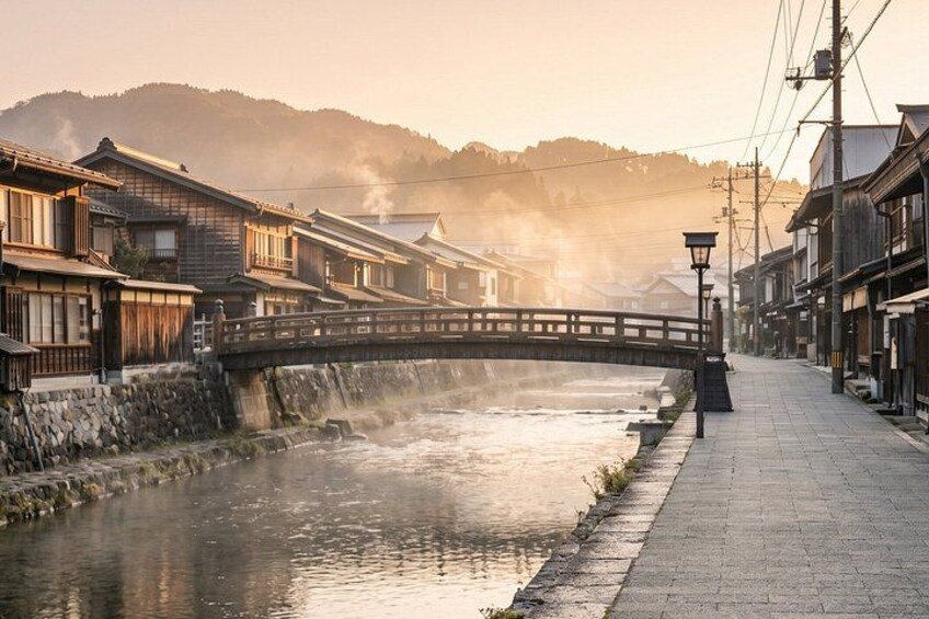 A traditional Japanese town with a stone bridge over a river, wooden houses, and a paved walkway. 2