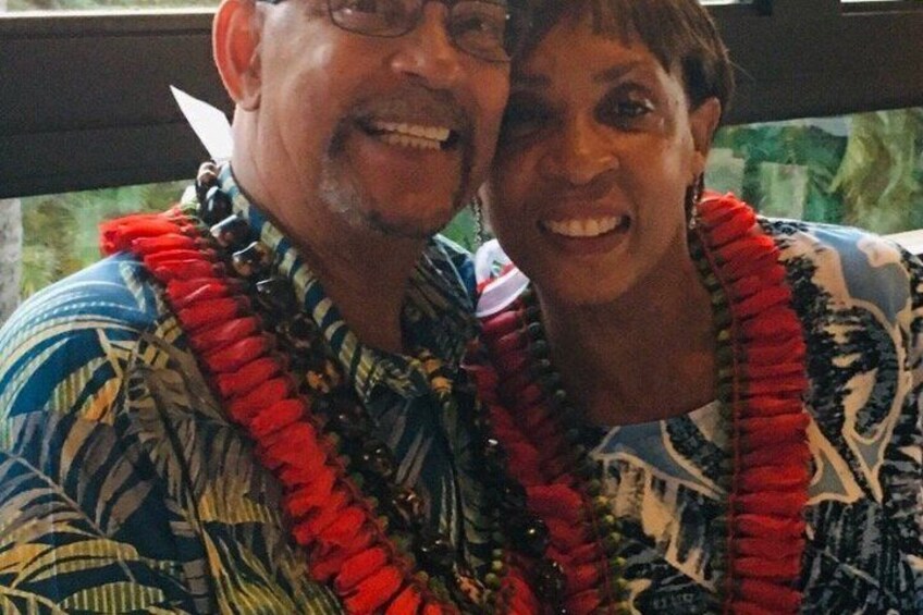 Two people wearing patterned shirts and red leis. 2