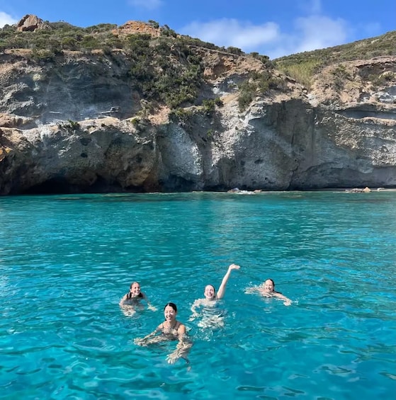 A group of people swimming in clear blue water with rocky cliffs in the background. 3