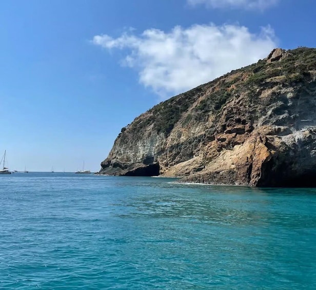 A coastal landscape with clear blue waters, a rocky cliff, and sailboats in the distance. 5