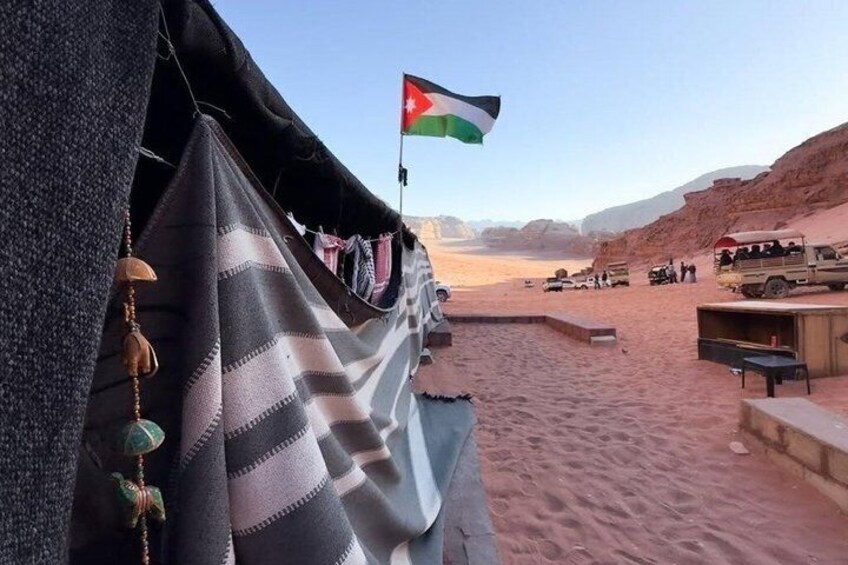 A desert landscape with tents, a flag, and vehicles. 2