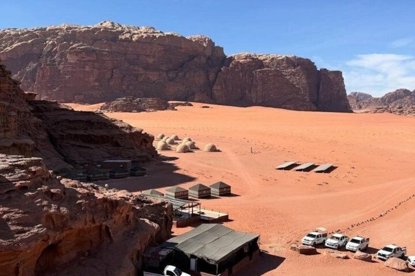 A desert landscape with rock formations, tents, and vehicles. 3