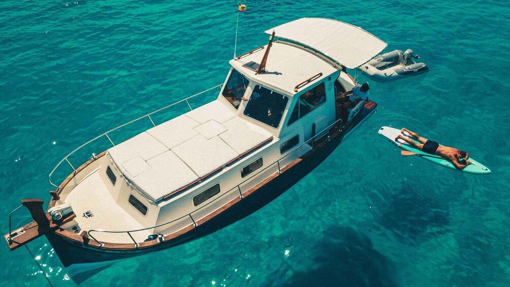 A boat with a covered deck and a person lying on a paddleboard nearby. 1