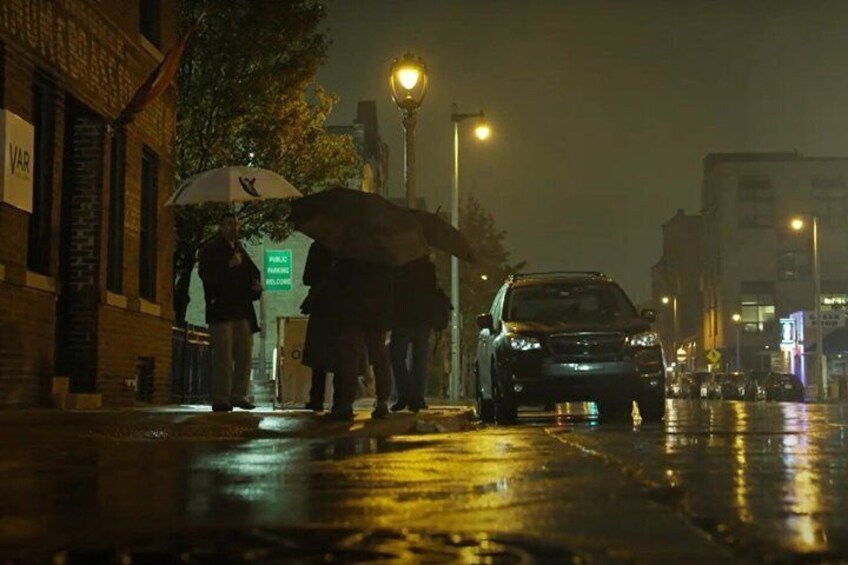 A wet street at night with a car parked on the side and a person holding an umbrella. 4