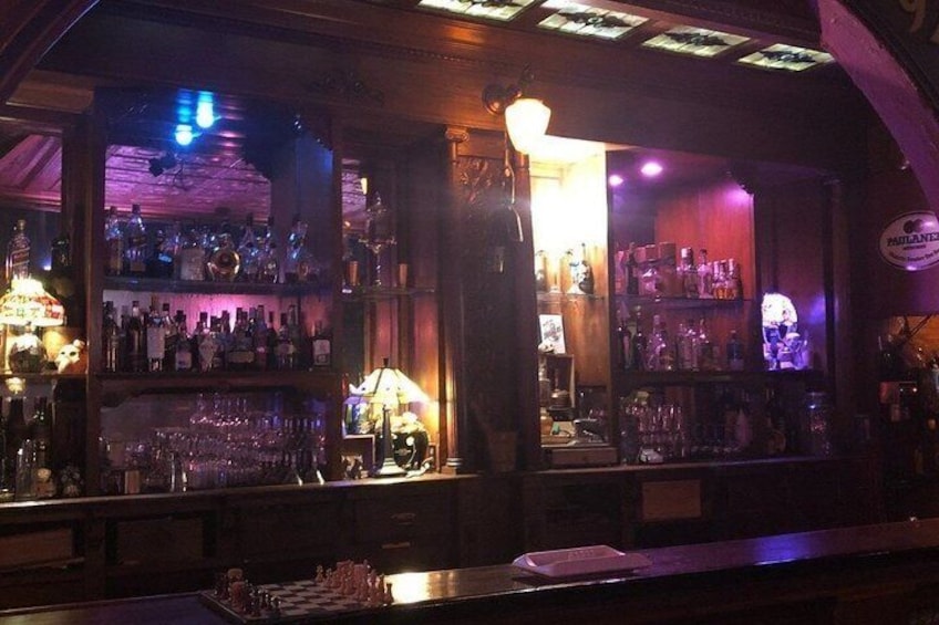 A bar with shelves of bottles and glasses, a counter with a cash register, and a sign reading 'Pauline's.' 3