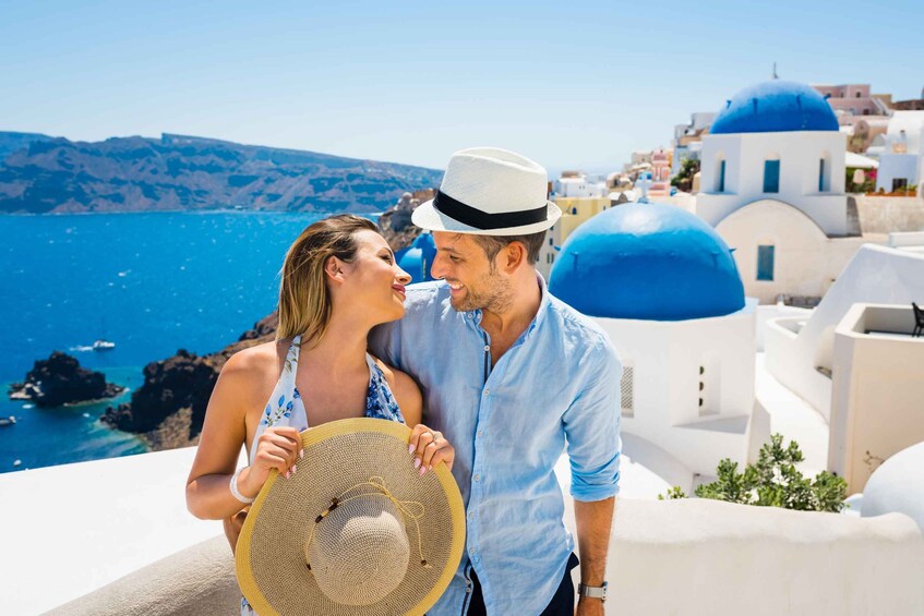 A couple on a balcony overlooking a coastal town with blue domed buildings and clear blue sea. 3