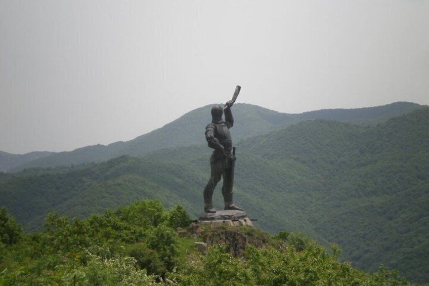 A statue of a person holding a flag on a hill with mountains in the background. 2