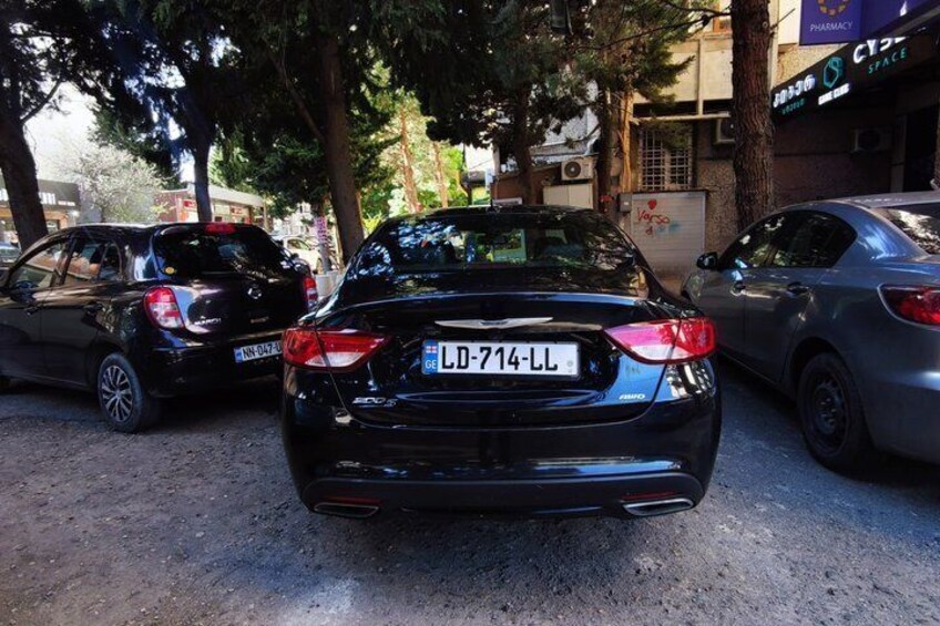 A black car with a visible license plate 'LD-714-LL' parked on a street with trees and buildings in the background. 5