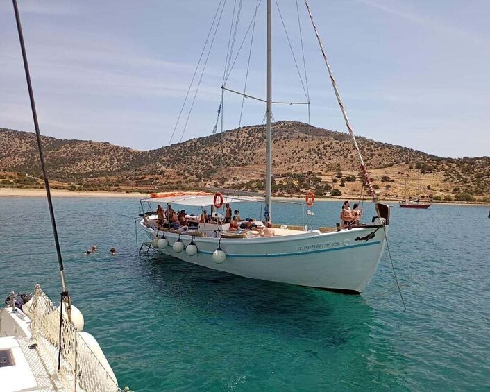 A sailboat docked at a calm harbor with clear turquoise water and a hilly landscape in the background. 1