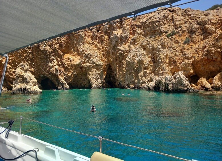 A boat in a turquoise sea with rocky cliffs in the background. 2