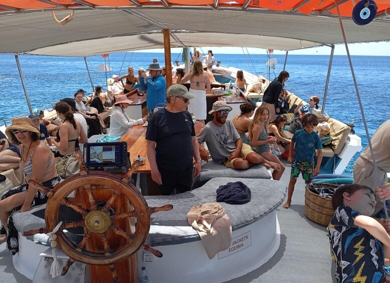 A crowded boat with people sitting and standing, a wooden steering wheel, and a canopy overhead. 3