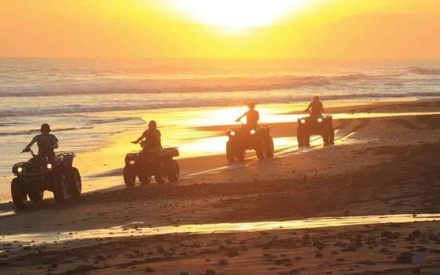 A sunset over a beach with four off-road vehicles parked on the sand. 2