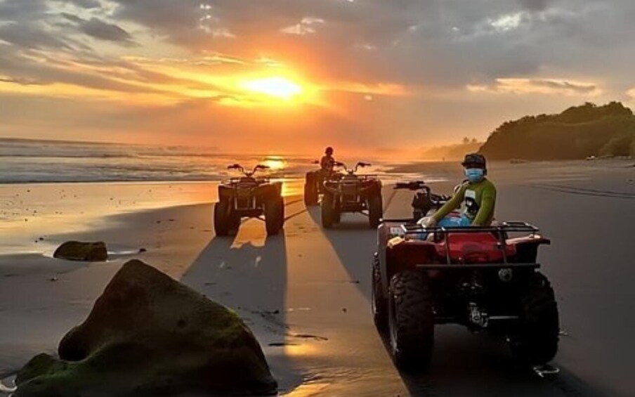 A sunset over a beach with ATVs parked in a line. 4