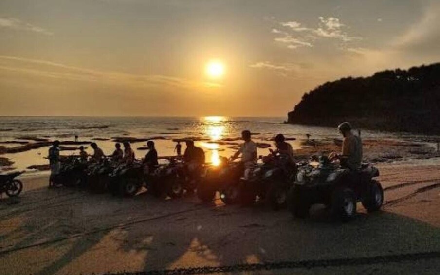 A sunset over a beach with people on quad bikes. 3
