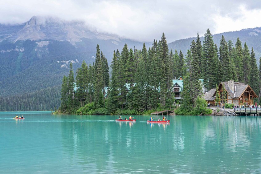 A calm lake with red canoes, a lodge, and a forested mountain backdrop. 3