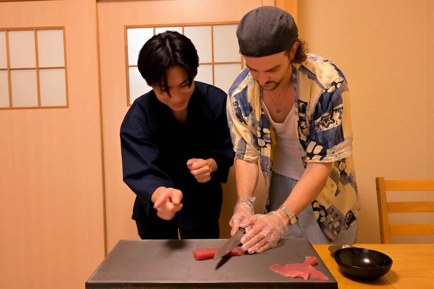 Two people cutting fish on a table in a room with traditional Japanese sliding doors. 5