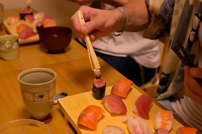 A person using chopsticks to pick up sushi from a wooden board. 3