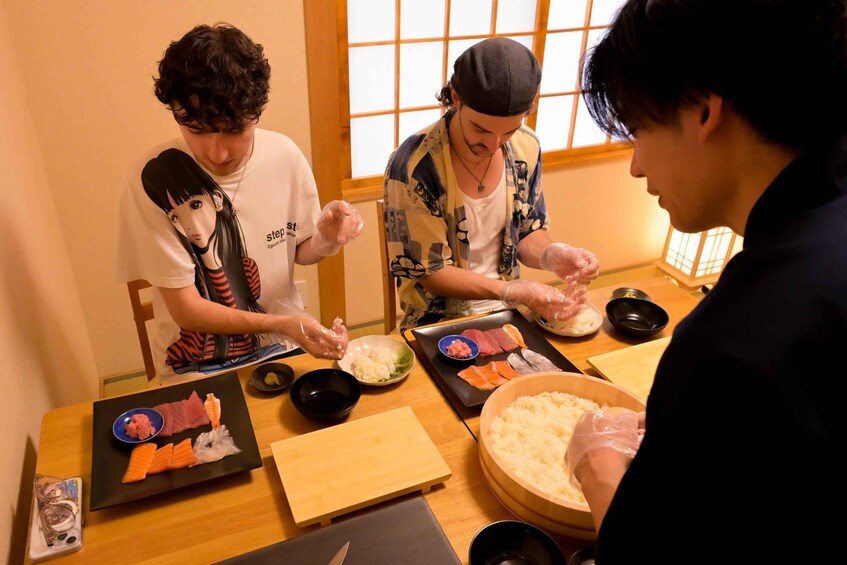 Three people preparing sushi at a table with various ingredients and tools. 4