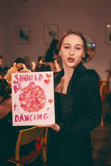 En person håller upp en skylt med ett hjärta i mosaik och orden ”BÖR DANSA”. 3