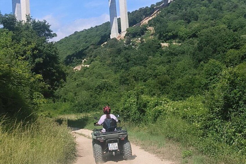 A person riding an ATV on a dirt path surrounded by lush greenery and hills. 4