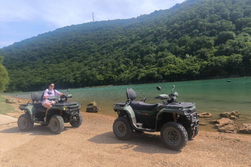 Two ATVs parked by a lake with a forested hill in the background. 3