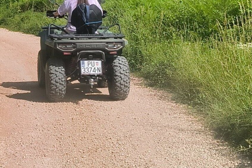 A person riding a green ATV on a gravel path with vegetation on the sides. 2