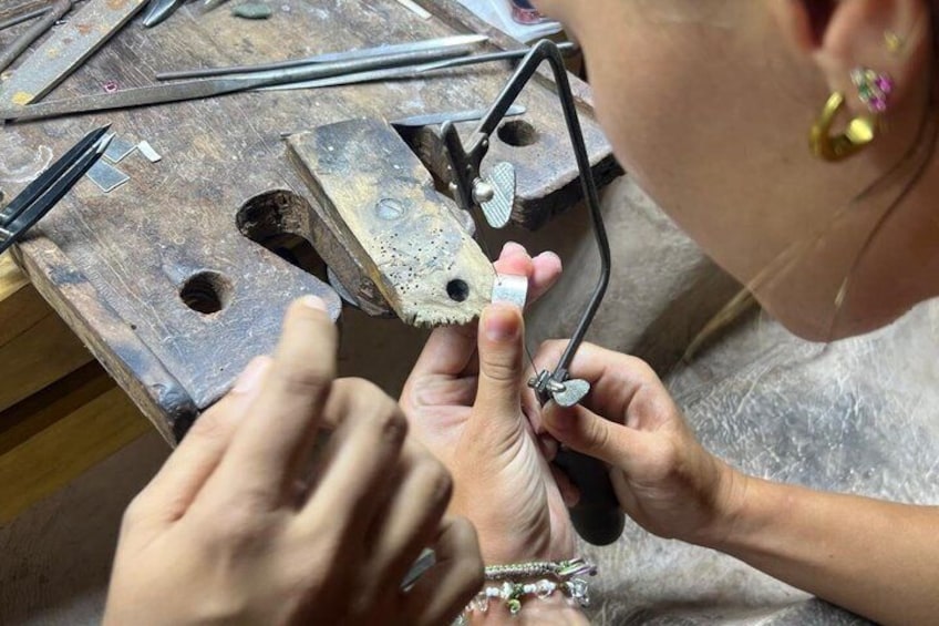 A person working on a metal piece with tools on a wooden workbench. 4