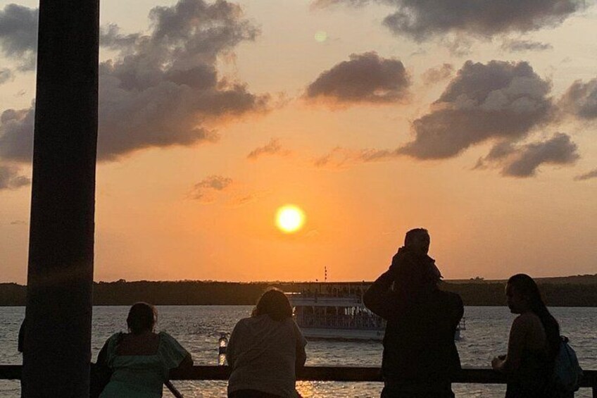 A sunset over a body of water with a pier and people silhouetted against the sky. 4