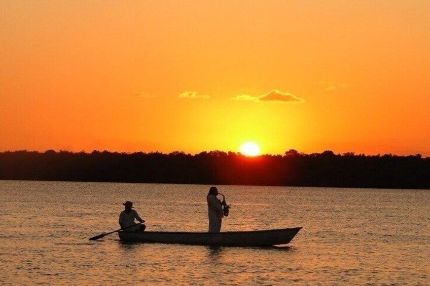 A sunset over a calm body of water with two people in a small boat. 2