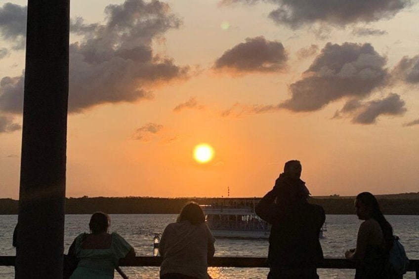 A sunset over a body of water with a pier and people silhouetted against the sky. 4
