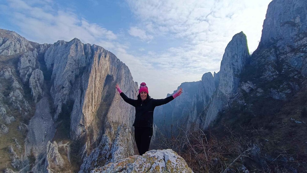 A person standing on a rock with arms outstretched, surrounded by rugged mountains. 1