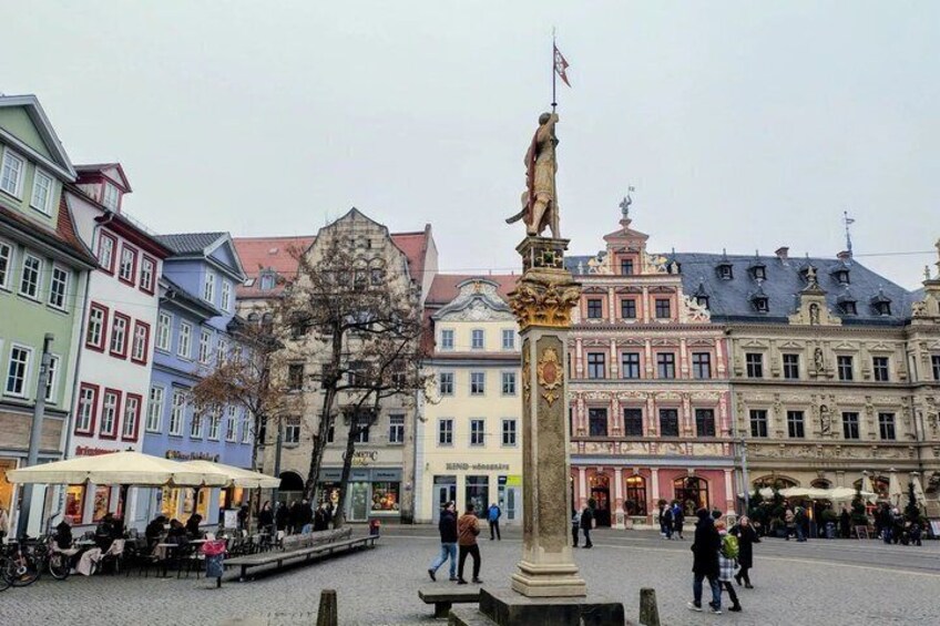 A square with a statue, historic buildings, and people walking. 1