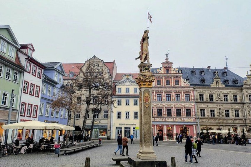 A public square with a statue, historic buildings, and people. 1