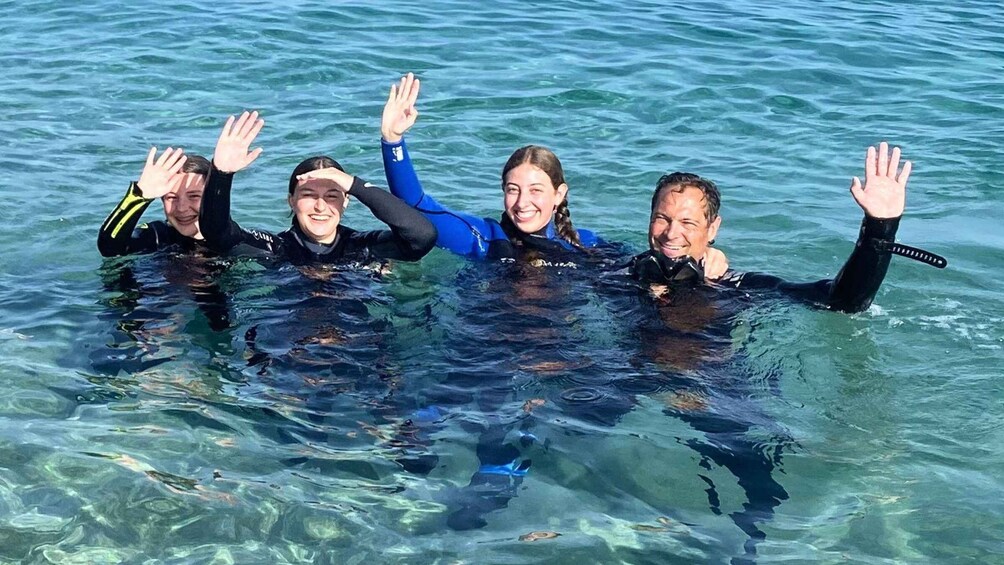 Four people in wetsuits swimming in clear water. 1