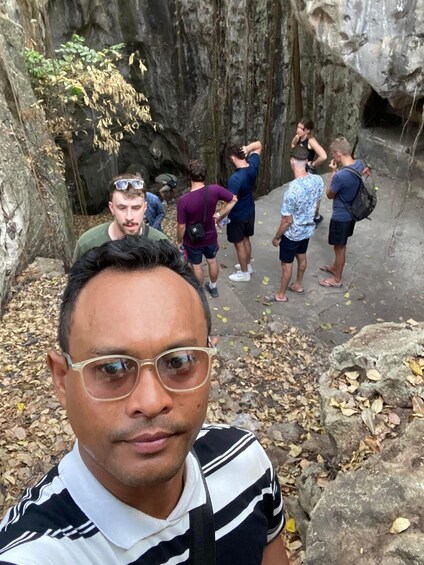 A group of people standing on a rocky path with a cave entrance in the background. 5