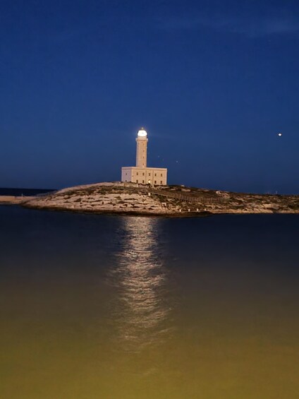 A lighthouse on a rocky outcrop with a calm sea in the foreground. 4