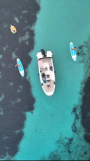 An aerial view of a boat anchored in turquoise waters with two paddleboards nearby. 1