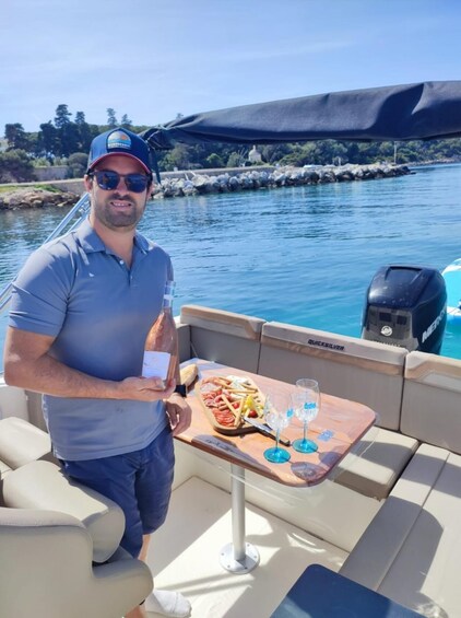 A man on a boat holding a bottle, with a tray of food and glasses on the deck. 4