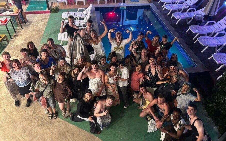 A group of people gathered around a pool area with lounge chairs and a 'WELCOME' sign. 1