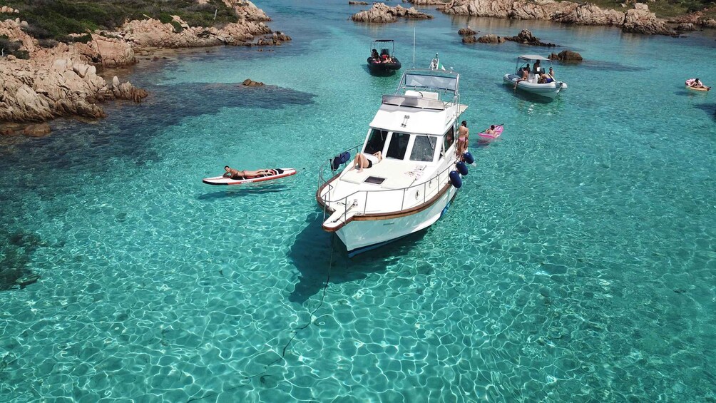 A clear turquoise sea with boats and a rocky shoreline. 1