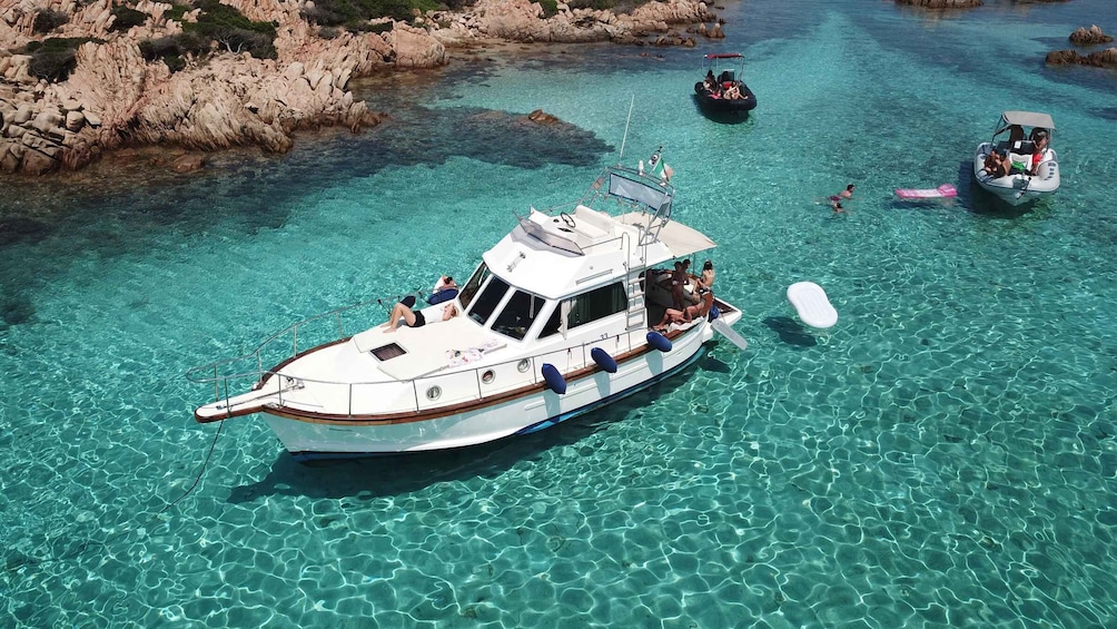 A white boat with passengers on a clear turquoise sea, surrounded by rocky cliffs. 3
