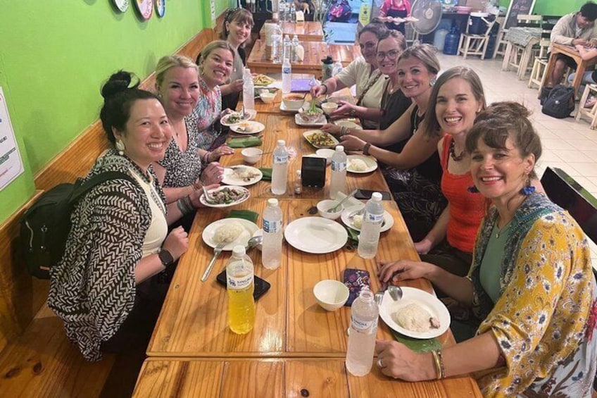 A group of people sitting around a wooden table in a restaurant with green walls. 1