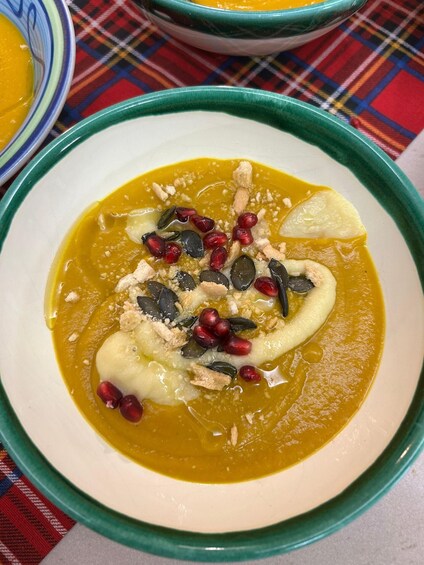 A bowl of pumpkin soup garnished with pomegranate seeds, pumpkin seeds, and crumbled nuts. 2