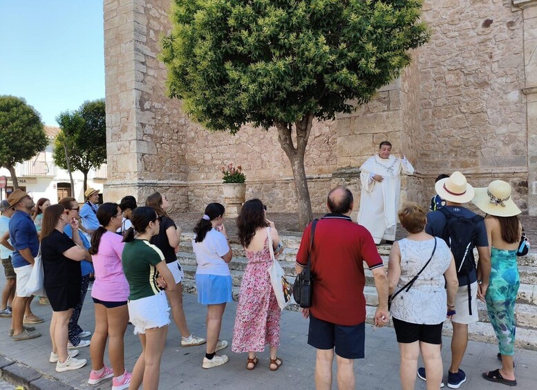 A group of people gathered in front of a stone building with a tree. 5
