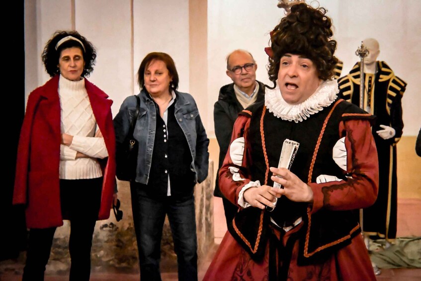 A group of people, one in a historical costume holding a book, standing in a room with a mannequin in the background. 3
