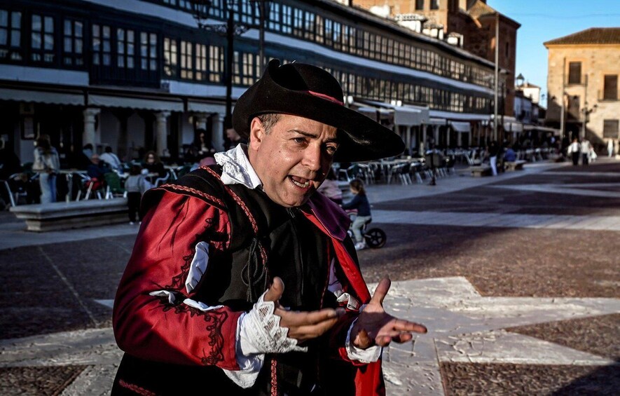 A person in historical costume standing on a city square with buildings in the background. 1