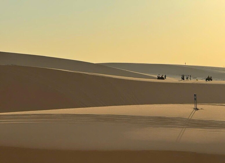 A desert landscape with sand dunes and a group of people and vehicles in the distance. 3