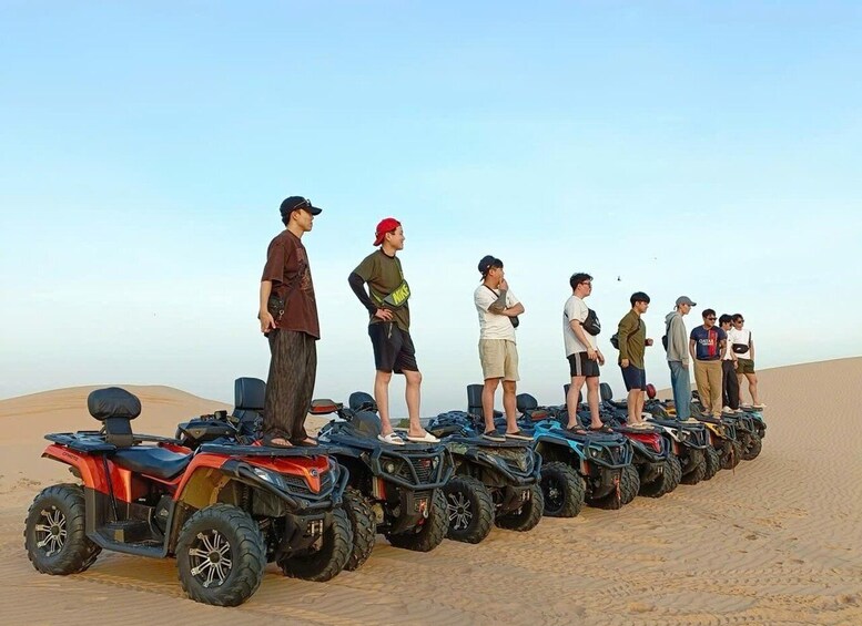 A group of people standing on ATVs in a desert. 1