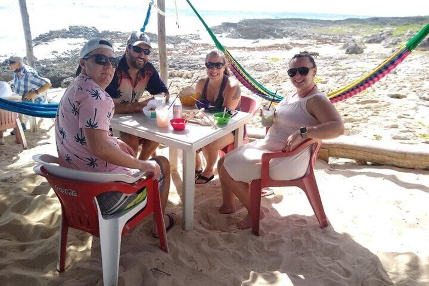 A group of people sitting at a table on a sandy beach with a hammock in the background. 1