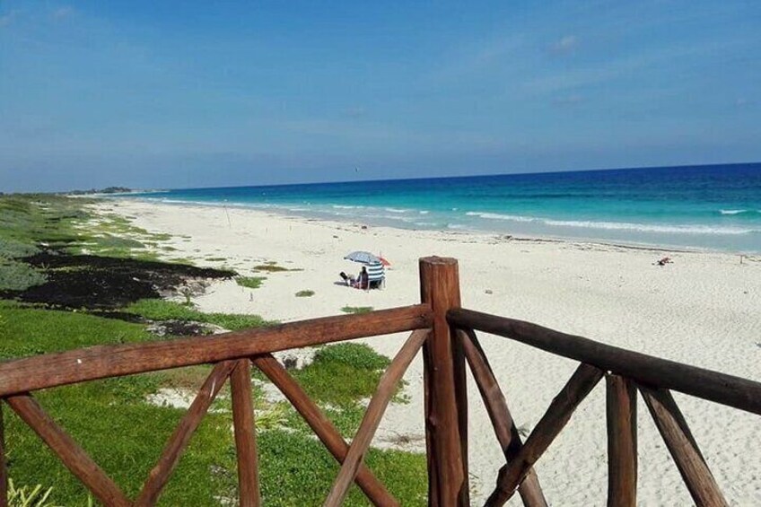 A beach with a wooden fence, clear turquoise water, and a few people in the distance. 5